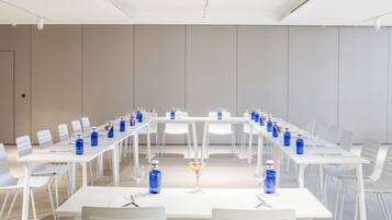 A conference room with white tables and chairs, blue water bottles, and a martini glass.