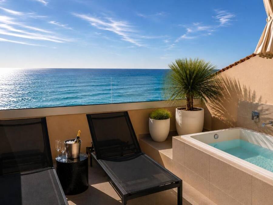 Varanda com vista para o mar, uma espreguiçadeira, uma mesa pequena com uma bebida, uma planta em vaso e uma banheira.