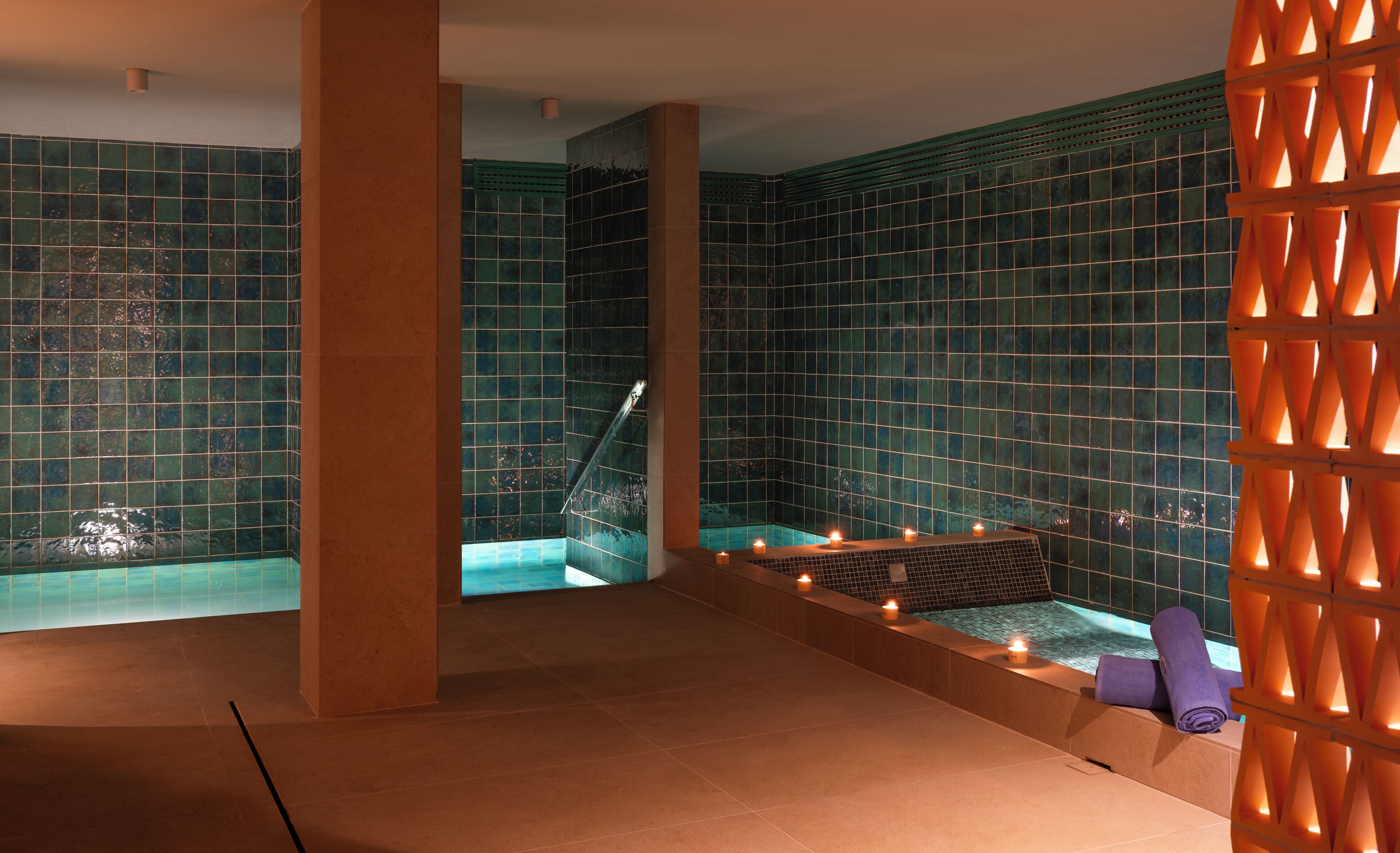 A spa area with a tiled wall, a bathtub, and candles.