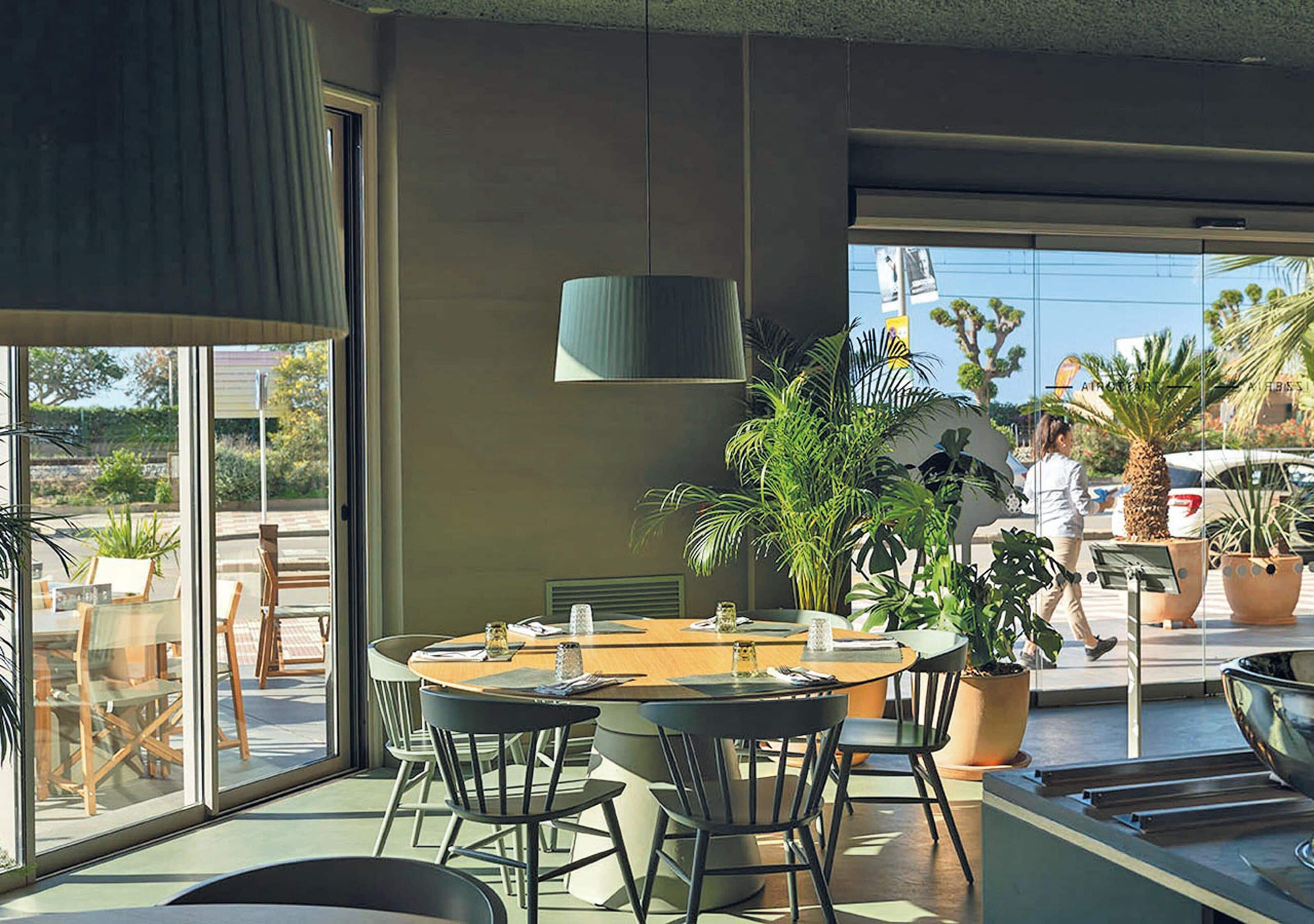 A modern dining area with a round table, chairs, and potted plants.