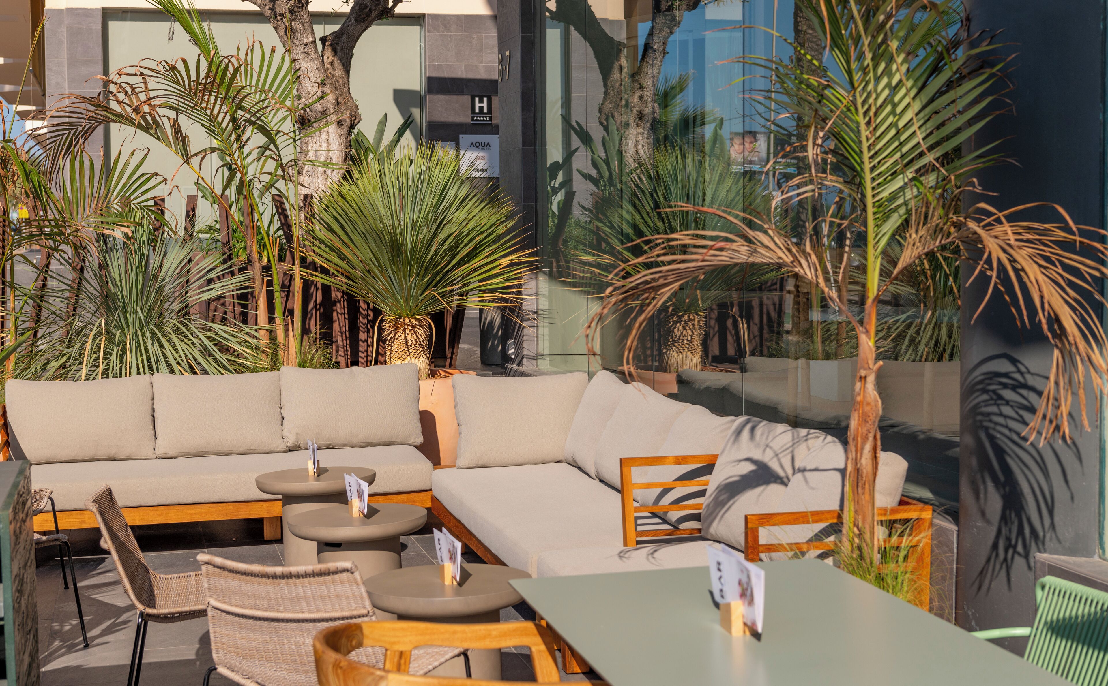 An outdoor seating area with a sofa, chairs, and tables, surrounded by potted plants.