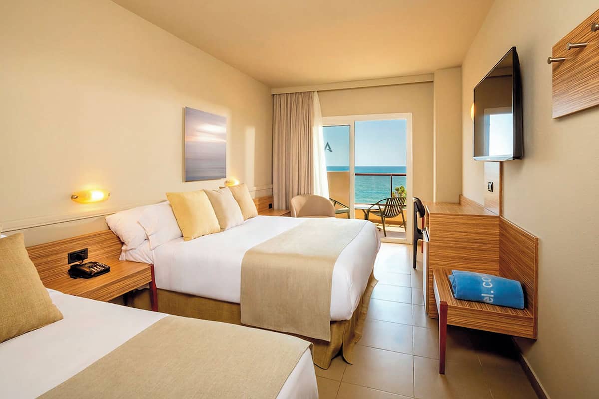 Une chambre d’hôtel avec deux lits, une télévision, un bureau et une vue sur la mer.