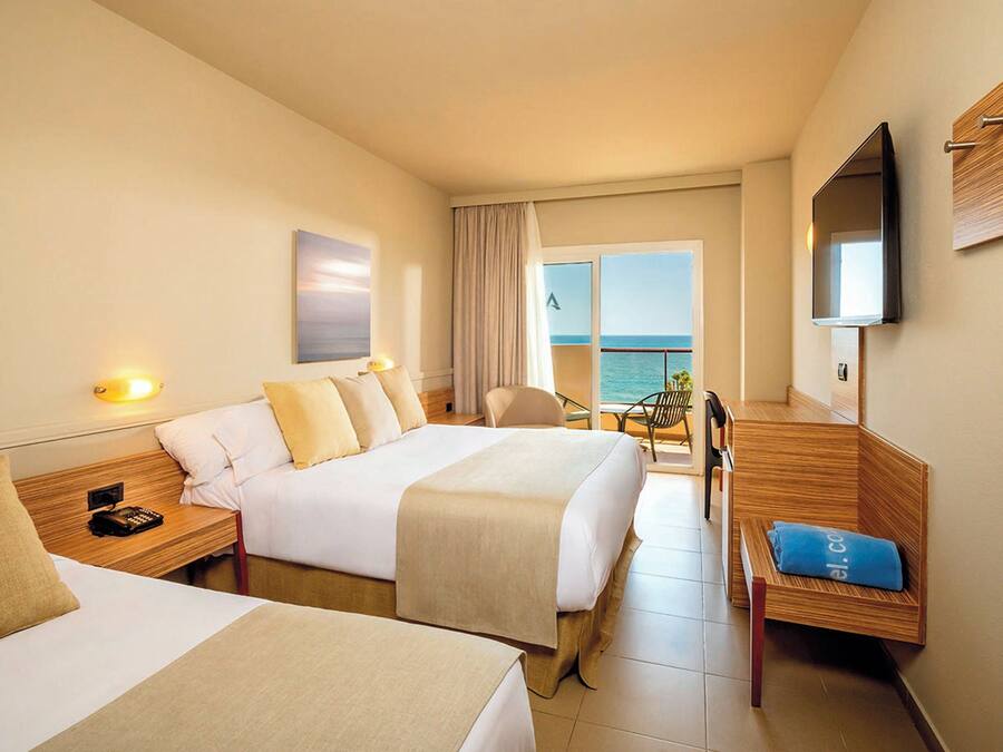 Habitación de hotel con dos camas, televisión, escritorio y vista al mar.