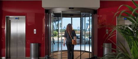 A revolving door with a red wall and a trash can beside it.