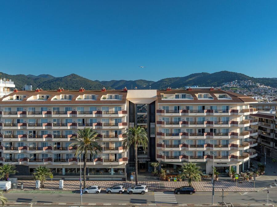 Un hotel de varios pisos con un atrio central, balcones y vistas del pueblo y las montañas circundantes.