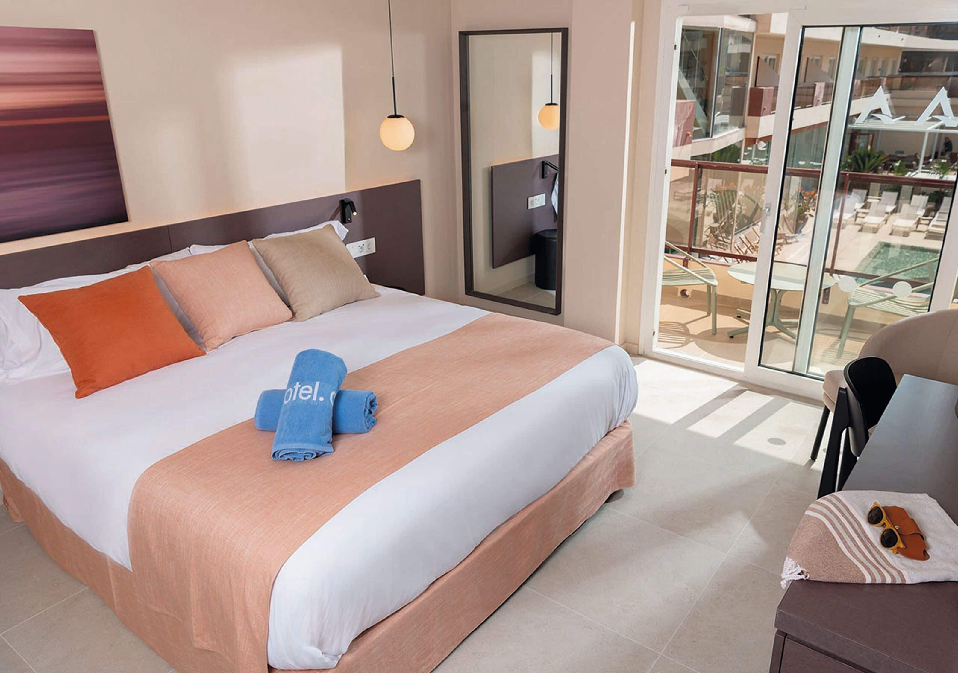 Ein Hotelzimmer mit einem großen Bett, einem Schreibtisch, einem Stuhl und einem Balkon mit Blick auf einen Pool.