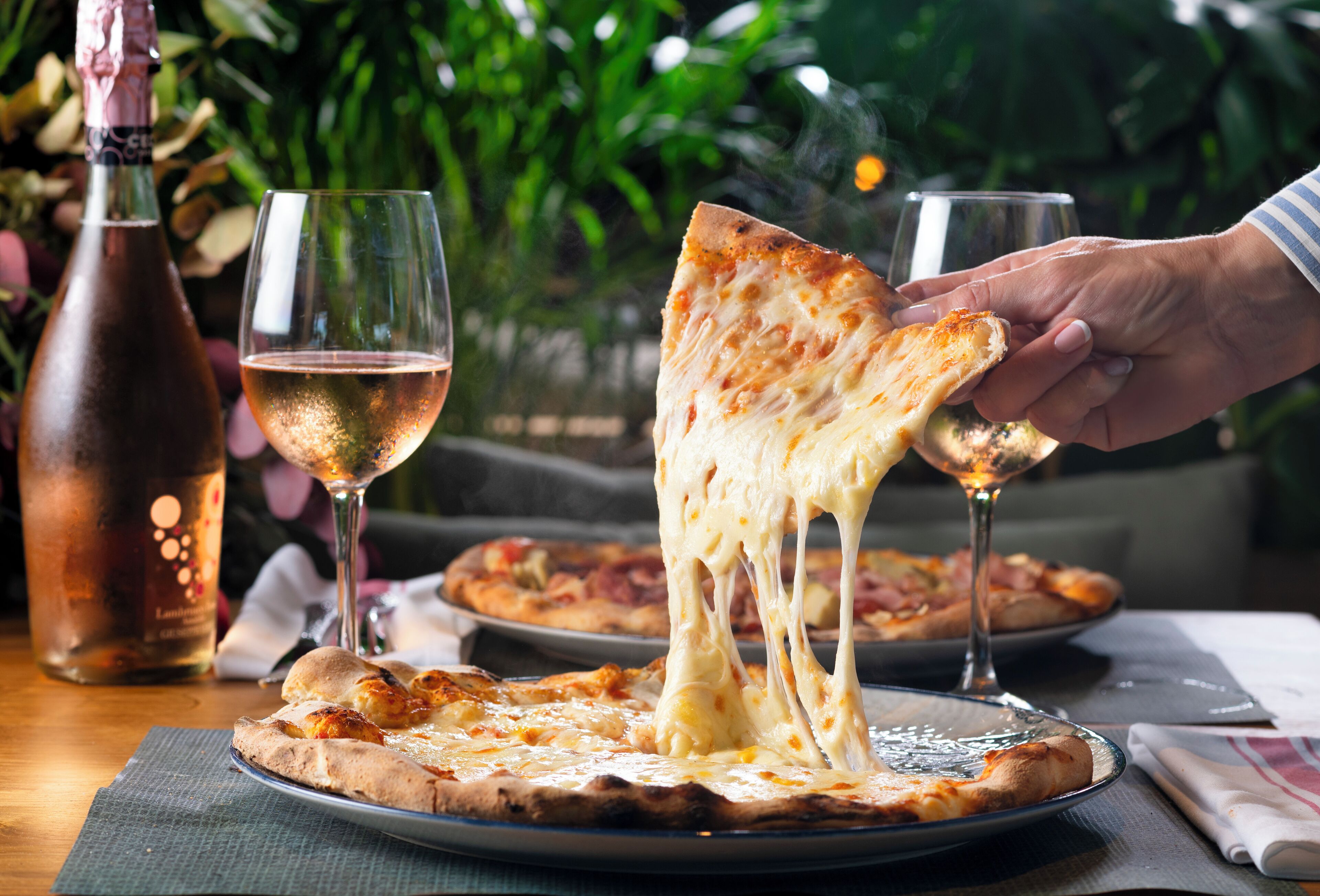 Una pizza con queso derretido, una botella de vino y una copa de vino sobre una mesa.