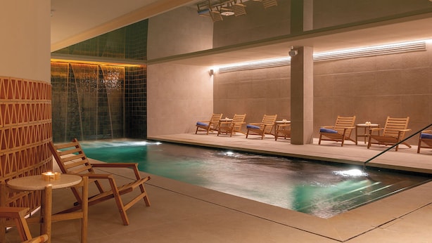 Una piscina interior con tumbonas de madera y pared de azulejos.