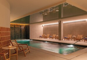 Une piscine intérieure dotée de chaises longues en bois et d’un mur carrelé.
