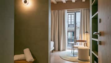Une chambre d’hôtel avec un lit, une petite table, une chaise, un tapis rond et un balcon avec des rideaux.