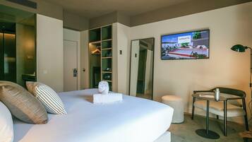 Quarto de hotel com cama, área de estar com uma cadeira, mesa pequena, televisão fixada na parede e armário com espelho.