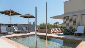 Un área de piscina en la azotea con sillones y sombrillas.