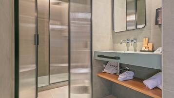 Un baño moderno con separador de vidrio, un lavamanos con espejo y un estante con toallas.