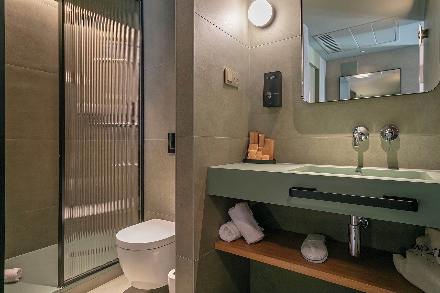 Un baño moderno con cabina de ducha de vidrio, inodoro, lavabo con espejo y perchero para toallas.