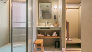 A modern bathroom with a large mirror, a sink, a wooden stool, and a trash bin.