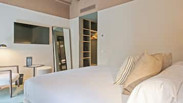 Una habitación de hotel moderna con una cama grande, un armario, un espejo, una mesita y una silla.