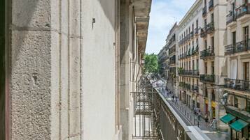 A view of a narrow street with buildings on either side, a metal railing, and pedestrians.