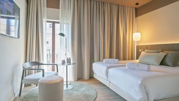 A hotel room with a bed, a desk, a chair, a round ottoman, and a view of the outside.