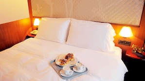 Una cama bien hecha con sábanas blancas, una bandeja con pasteles y café, y lámparas de noche.