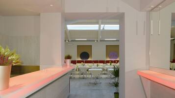 A modern hotel lobby with a reception desk, multiple seating areas, and a view of the dining area.
