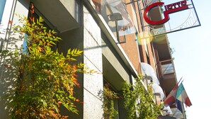 Un edificio con un gran letrero rojo, un toldo de vidrio y algo de vegetación.