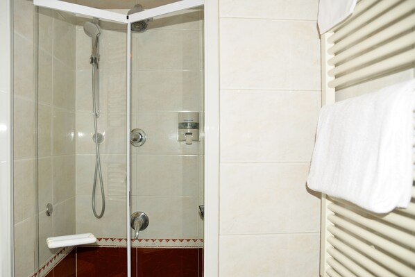 Ducha con mampara de vidrio, cabezal de ducha manual y panel de control en la pared.