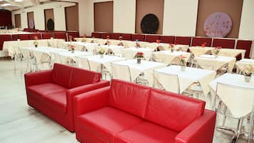 Ein geräumiger Festsaal mit Tischen und Stühlen, einem roten Sofa und dekorativen Wandbildern.