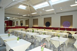Un'ampia sala da pranzo con numerosi tavoli e sedie, soffitti alti con lucernari e decorazioni alle pareti.