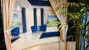 Una habitación con un ventanal grande, dos sillones azules, un tapete estampado y una planta en maceta.