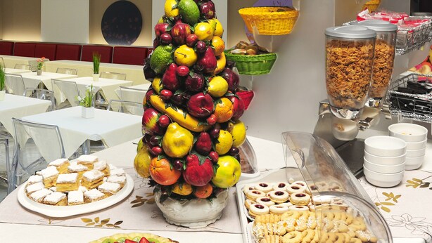 Un bufé con diversos alimentos, que incluye un centro de mesa con frutas, pastelería y una tarta de frutas.