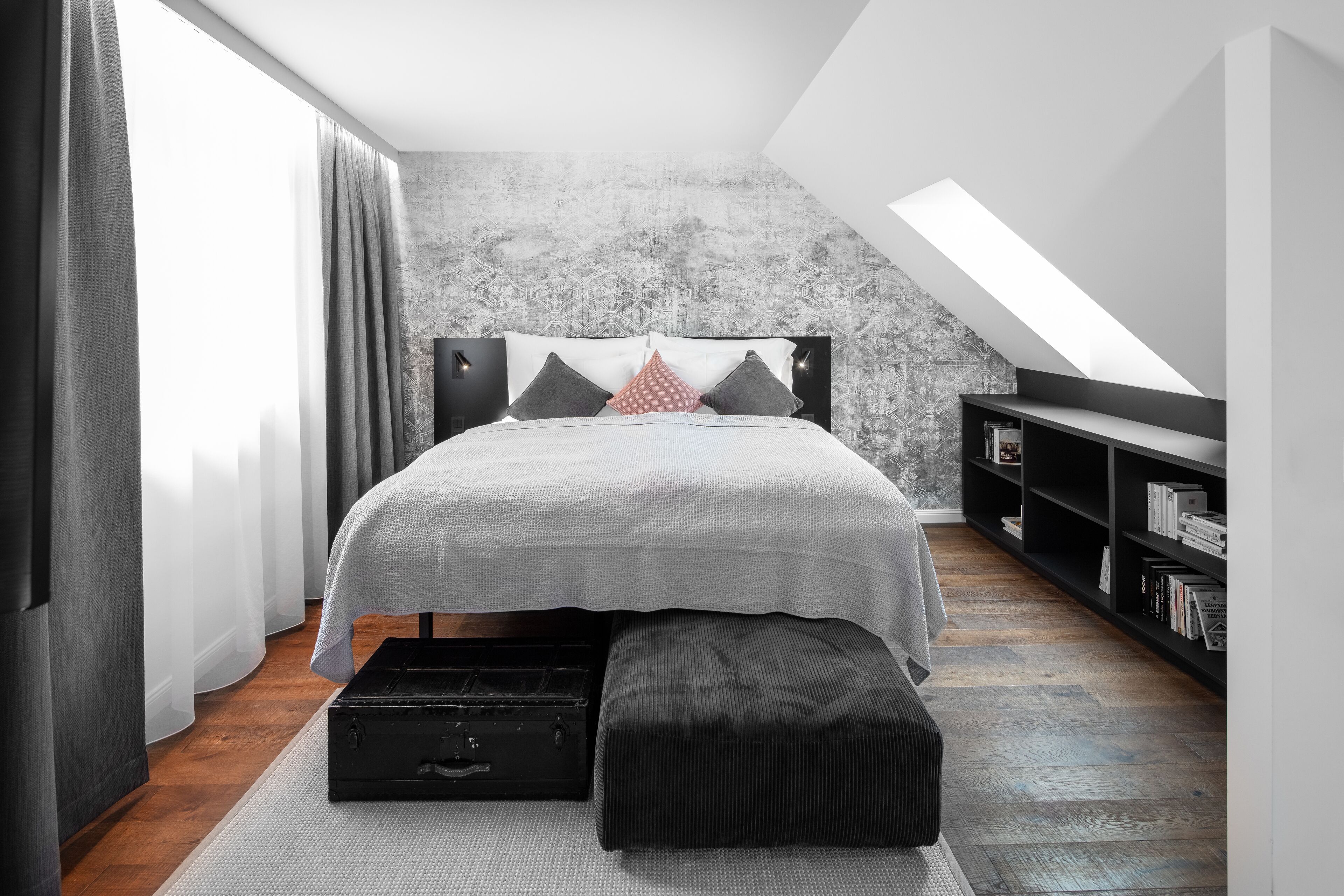 Quarto moderno com cama, um banquinho, estante e claraboia.