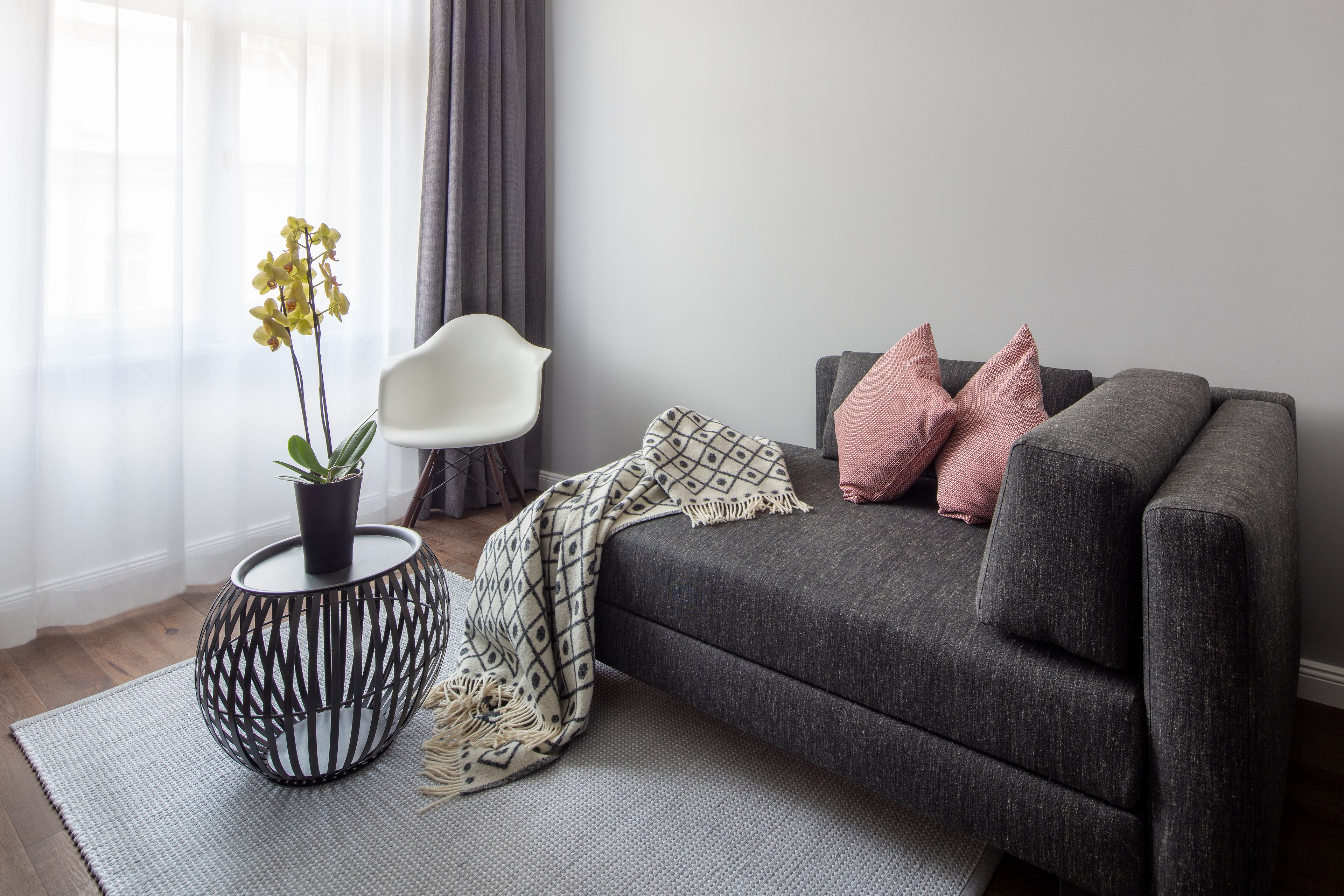 Una sala de estar moderna con un sofá gris, una silla blanca, una manta estampada y una planta en una mesa redonda.