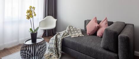 Una sala de estar moderna con un sofá gris, una silla blanca, una manta estampada y una planta en una mesa redonda.