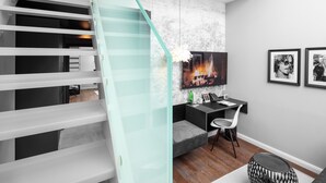 Ein modernes Interieur mit einer Treppe, einem Schreibtisch mit Stuhl, einem Fernseher und gerahmten Bildern an der Wand.
