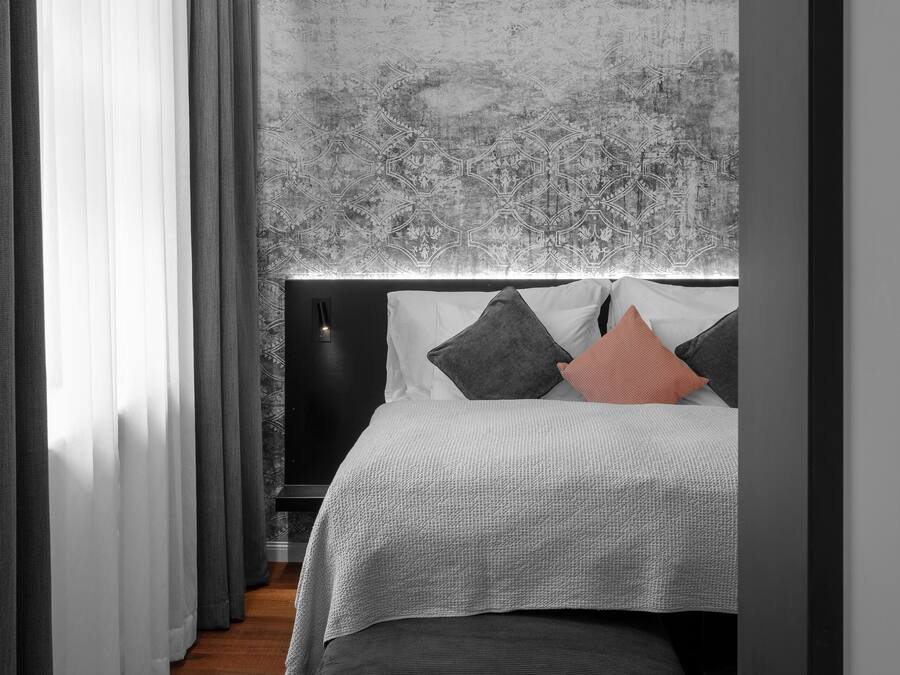 A modern bedroom with a large bed, a headboard with a textured wall, and a window with sheer curtains.
