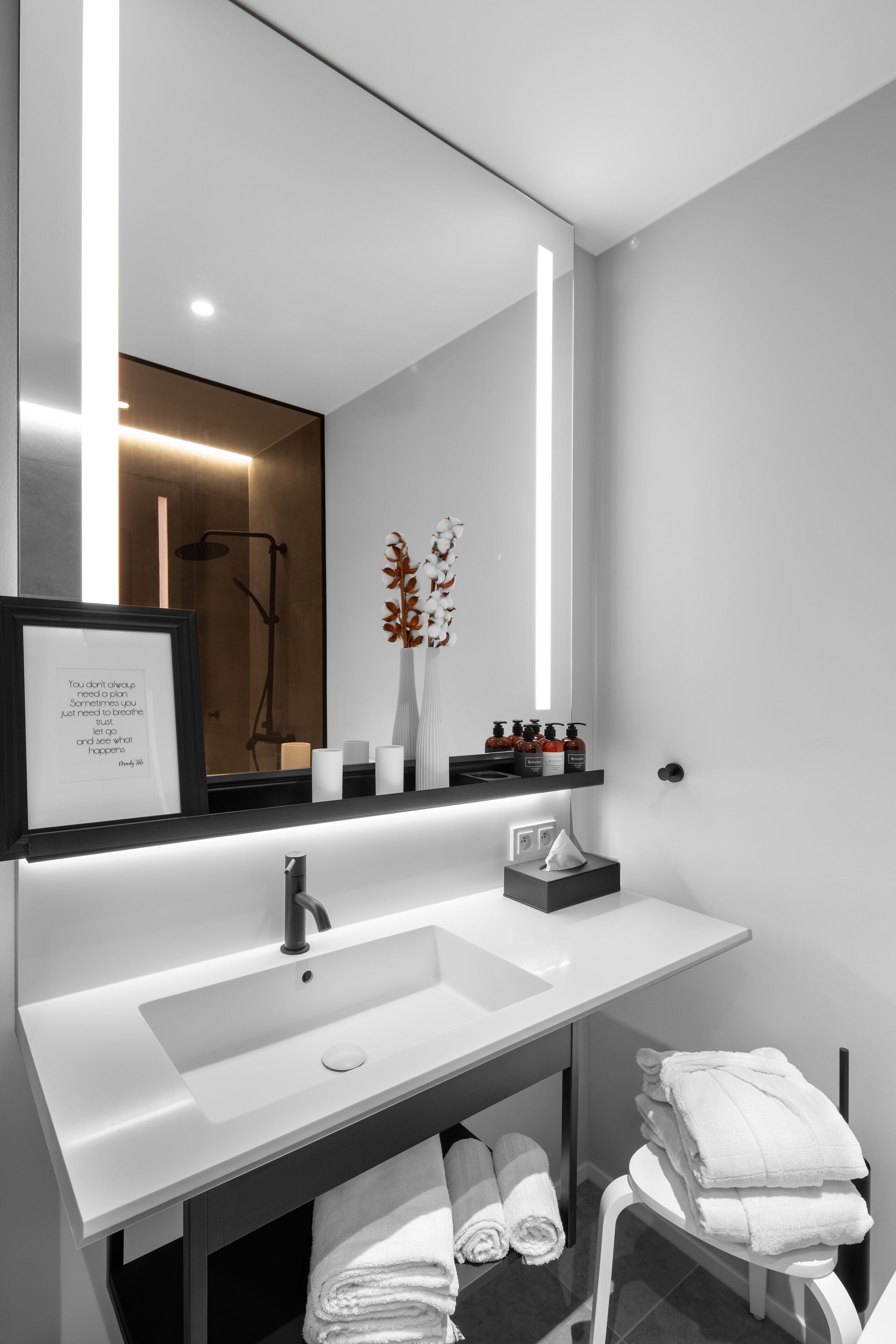 Un baño moderno con un lavamanos blanco, un espejo grande y una cita enmarcada en la pared.
