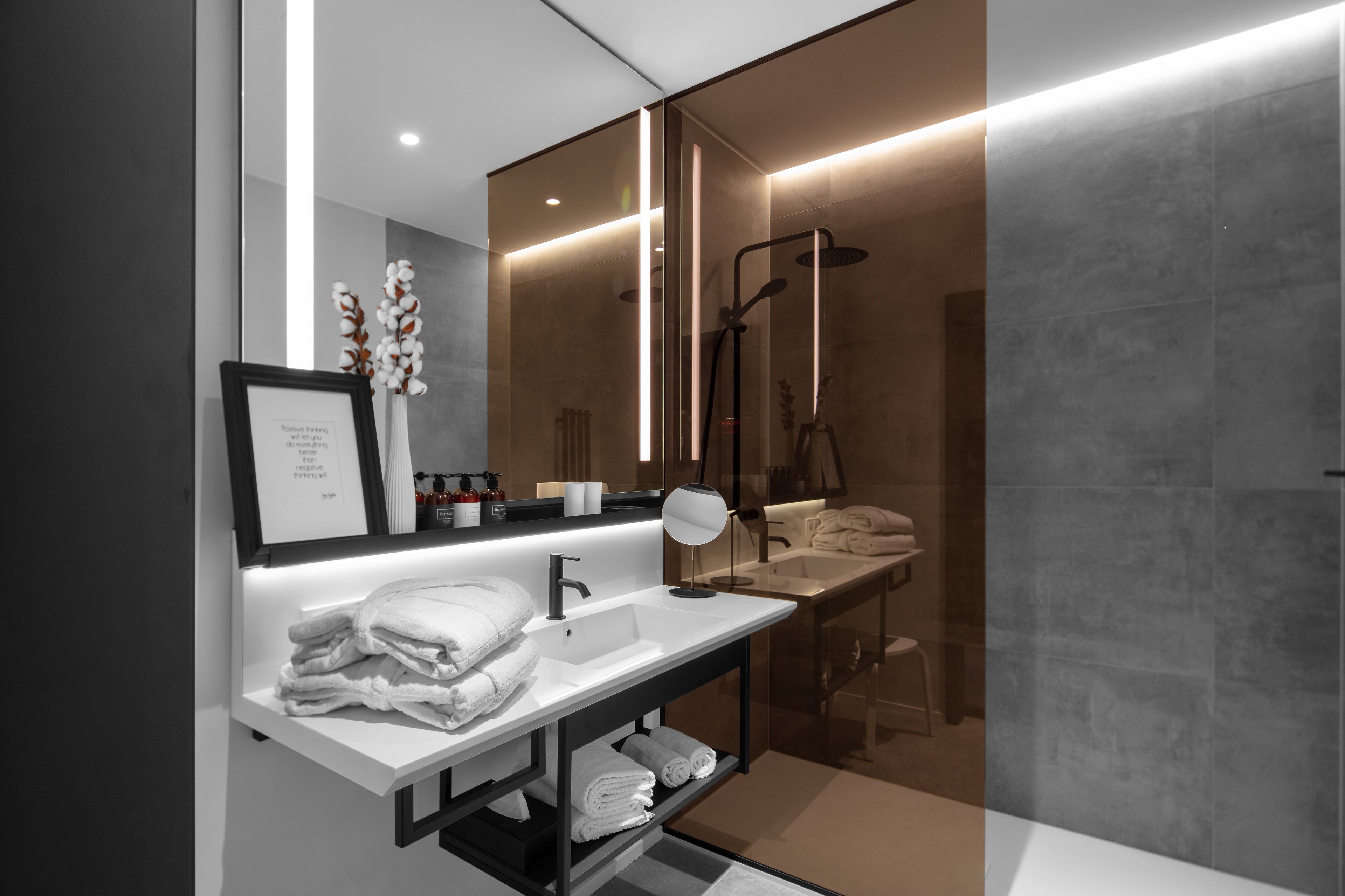 A modern bathroom with a glass-enclosed shower, a white vanity with a mirror, and neatly folded towels.