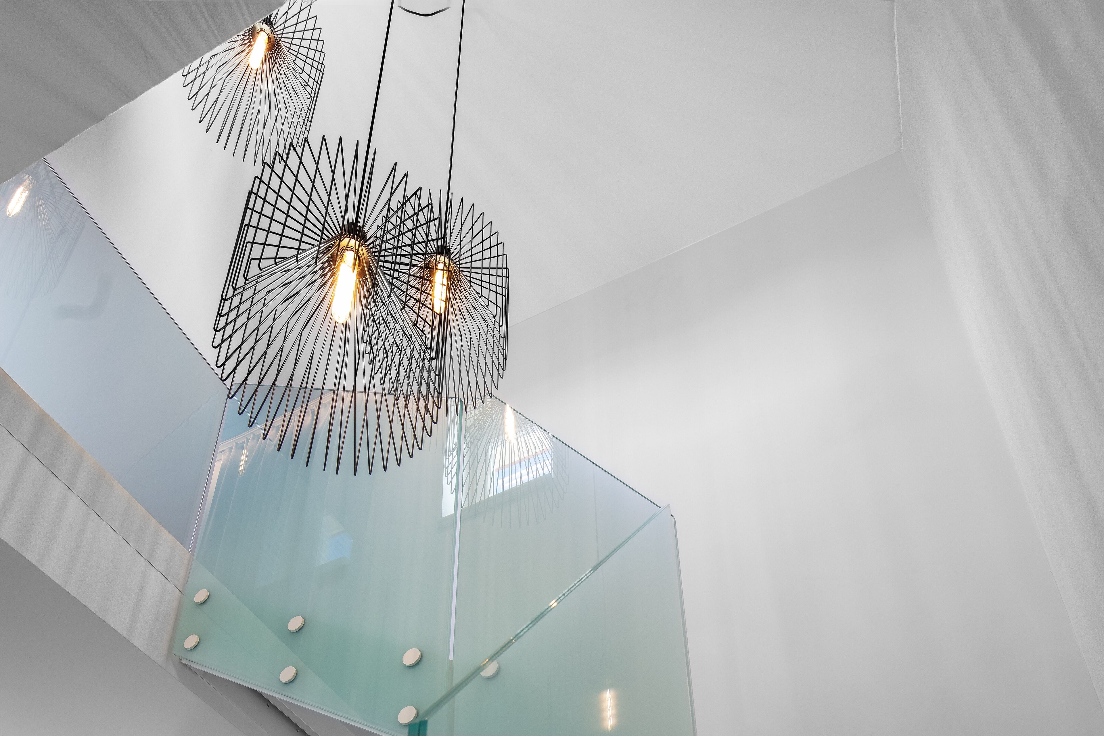 Un interior moderno con una escalera de cristal y lámparas de techo con diseños geométricos.