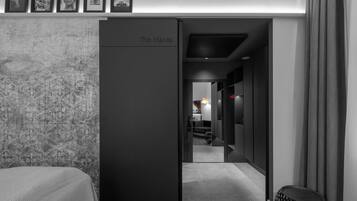 Moderni hotellihuone, jossa on suuri vaatekaappi, kuvioitu tapetti ja käytävä, joka johtaa ruokailutilaan.