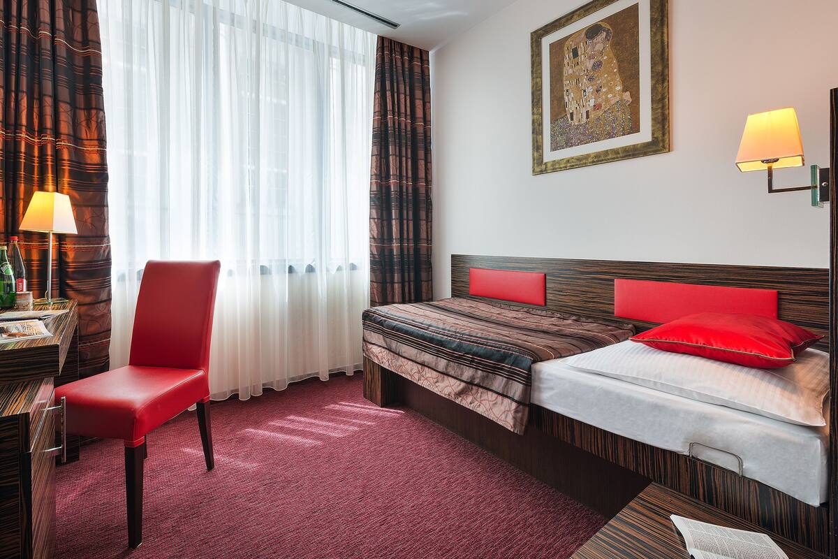 A hotel room with a bed, a chair, a desk, and a window with curtains.