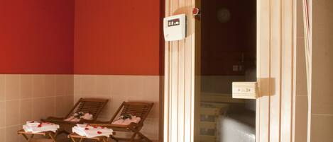 A spa room with two wooden loungers, a red wall, and a glass door leading to a bathroom.