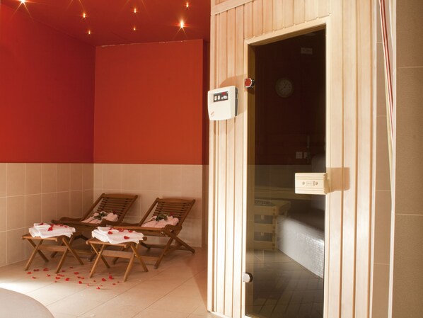 Une salle de spa avec deux chaises longues en bois, un mur rouge et une porte en verre donnant sur une salle de bain.
