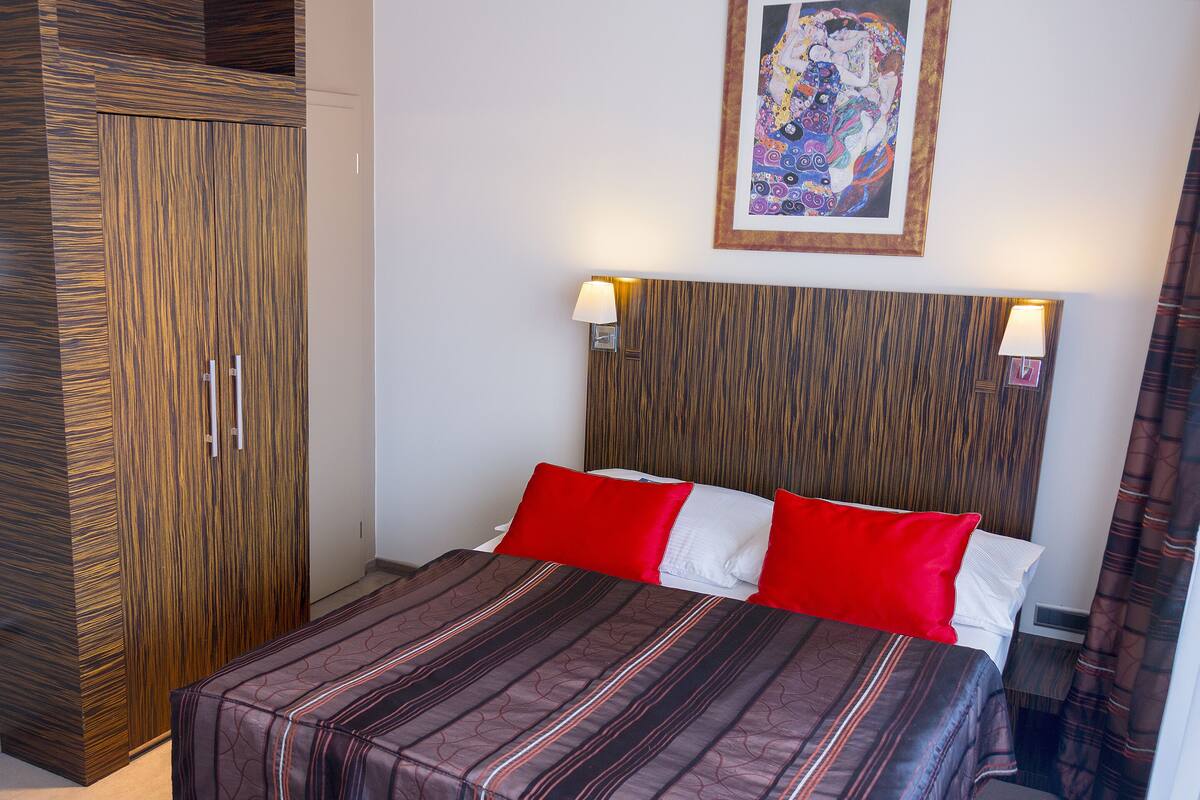 A hotel room with a bed, a wardrobe, and a painting on the wall.