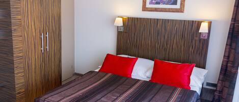 A hotel room with a bed, a wardrobe, and a painting on the wall.