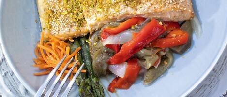 Un plato con un filete de salmón, espárragos, pimientos rojos y rodajas de limón.