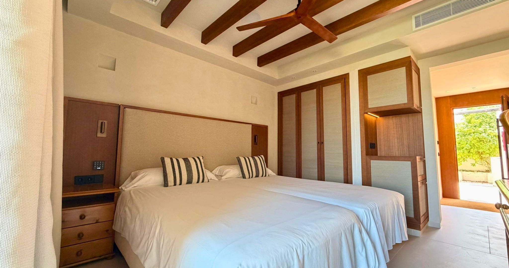 A bedroom with a large bed, wooden headboard, a nightstand, a wardrobe, and a door leading to a balcony.
