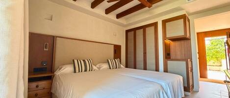 A bedroom with a large bed, wooden headboard, a nightstand, a wardrobe, and a door leading to a balcony.