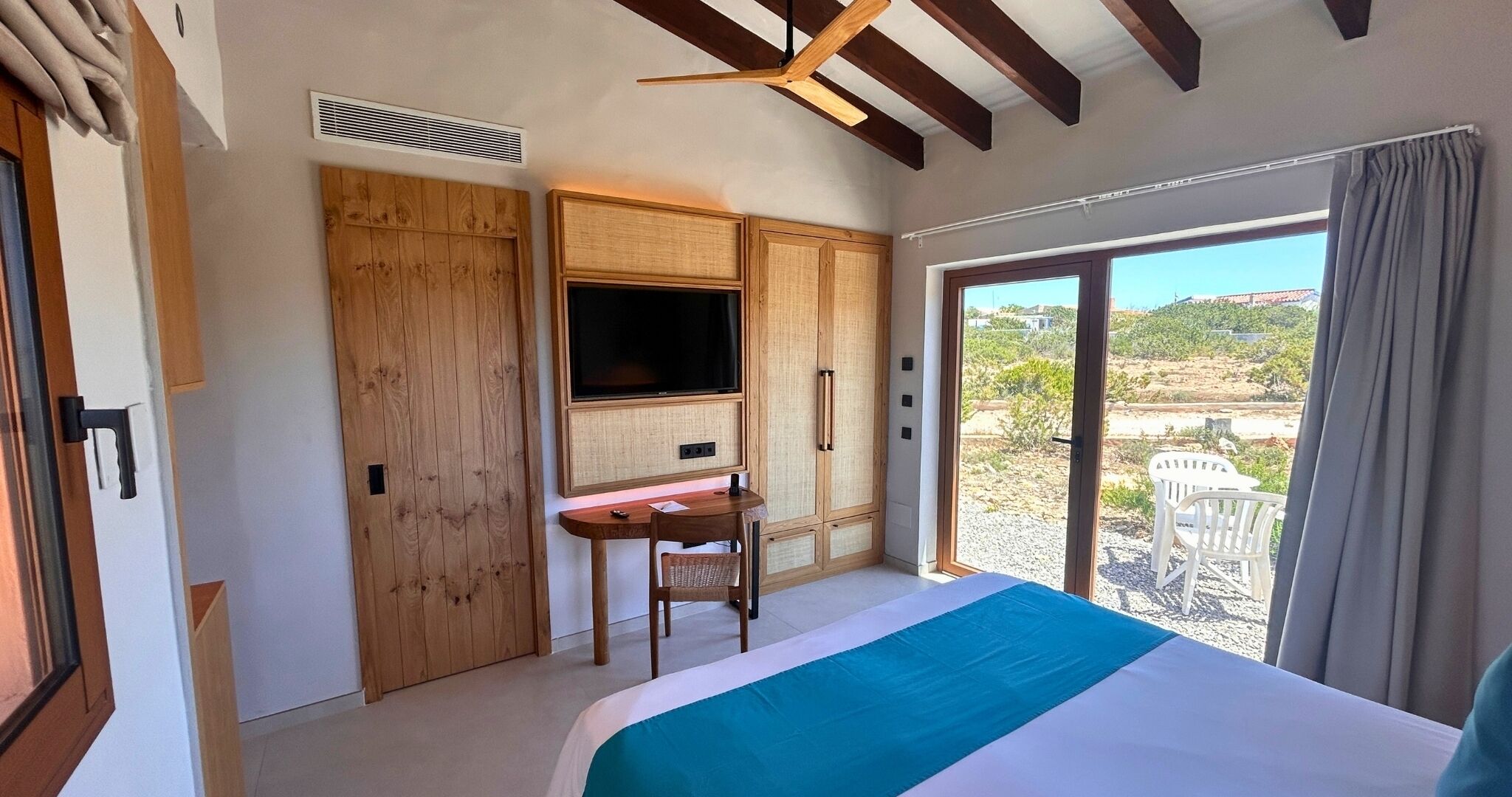 Een slaapkamer met een bed, een bureau, een televisie en een schuifdeur naar een balkon.