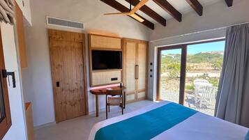 A bedroom with a bed, a desk, a TV, and a sliding glass door leading to a balcony.