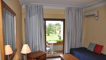 Camera d'albergo con un letto, un tavolo, una sedia, una lampada, un tavolino rotondo con una sedia e vista su un giardino attraverso una porta.